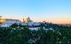 A blue sky and green trees frame a sunrise view of Madrid's cathedral and Royal Palace.